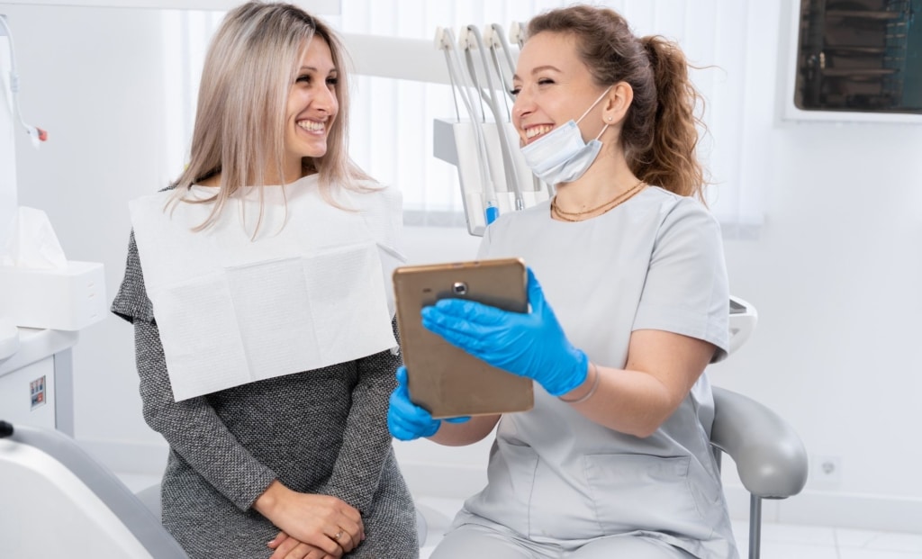 Dentist using a tablet to review treatment details with a smiling patient, showcasing cloud-based Practice Management Software.